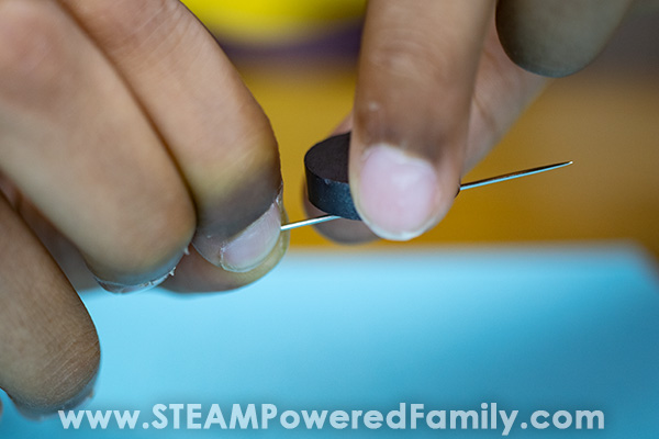 A close up of a child's fingers as they use a magnet to create a magnetic charge on a needle by moving it along the needle to create a homemade compass