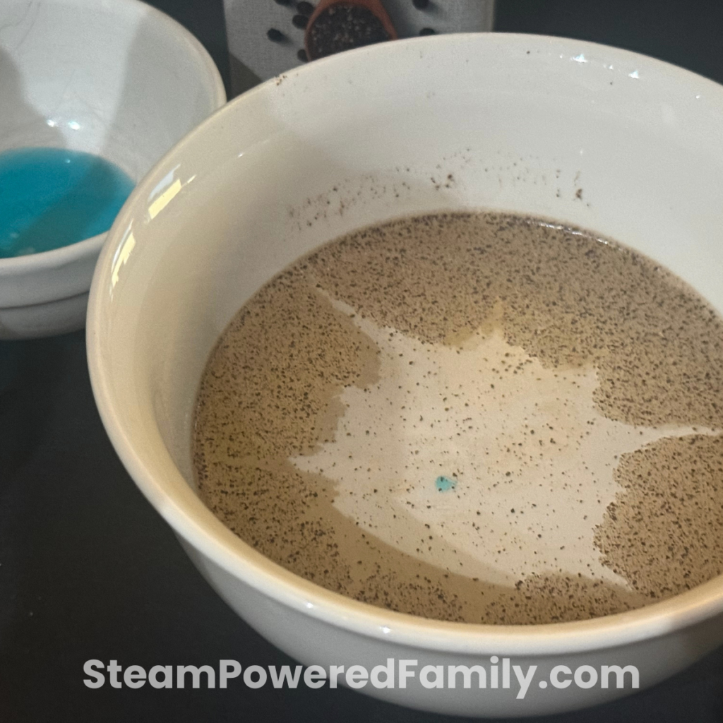Black pepper scattering across a shallow bowl of water after a soapy cotton swab touches the surface in a no prep water STEM activity.